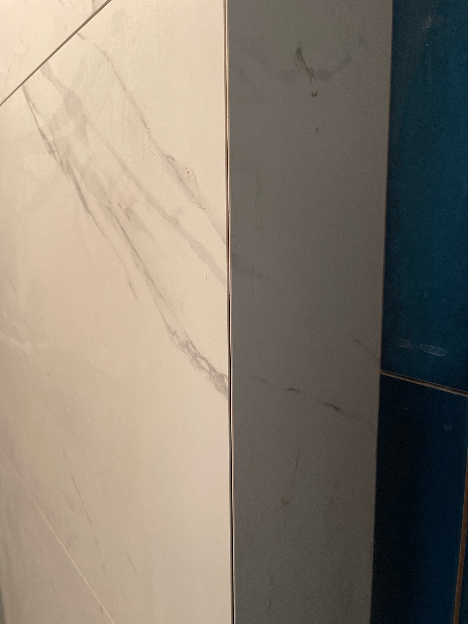 Połączenie płytek: białe marmurowe i granatowe, tworzące kontrastowe wykończenie ściany. Widoczne delikatne żyłki marmuru i gładka powierzchnia płytek.