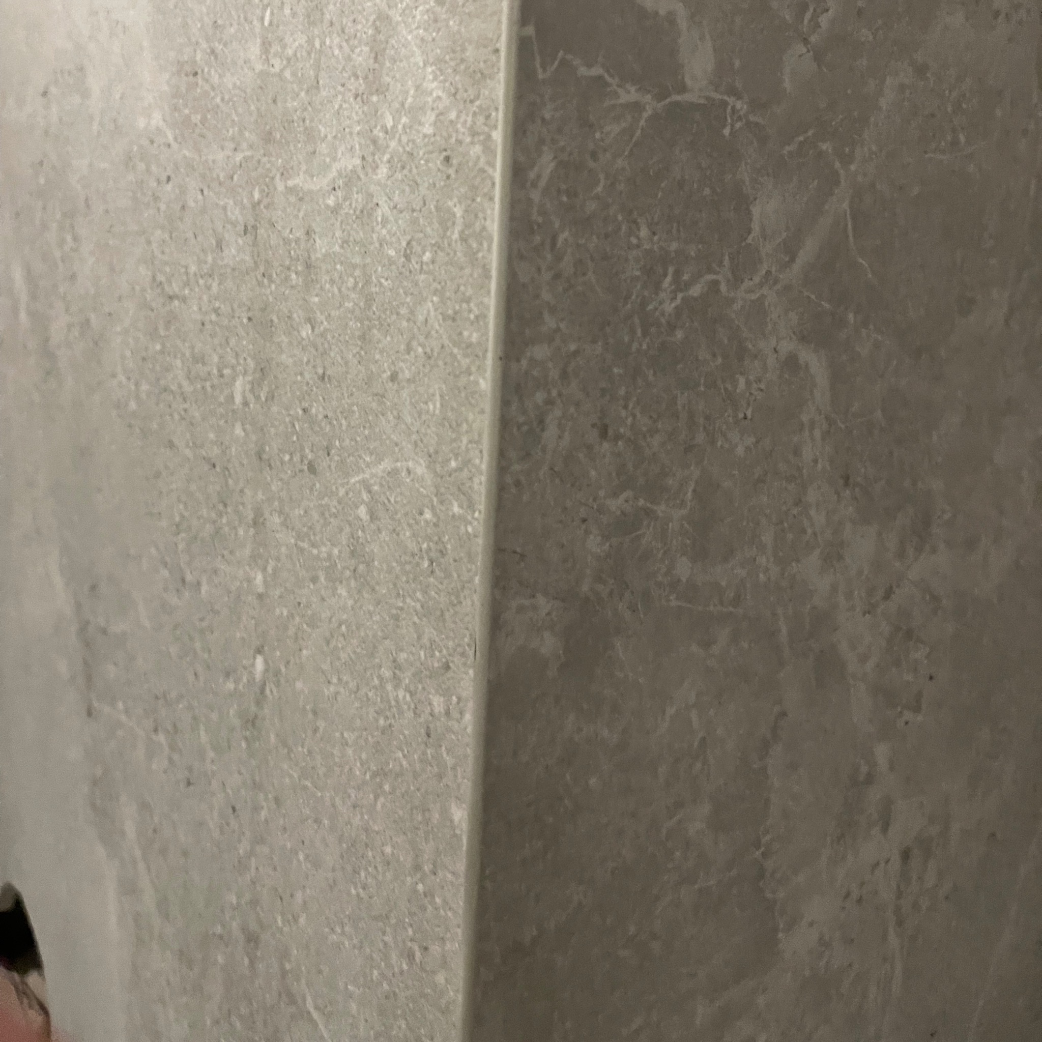 Szare, marmurkowe płytki ceramiczne ułożone na rogu ściany, z widoczną fugą. Minimalistyczny design, neutralna kolorystyka, bliski kadr.