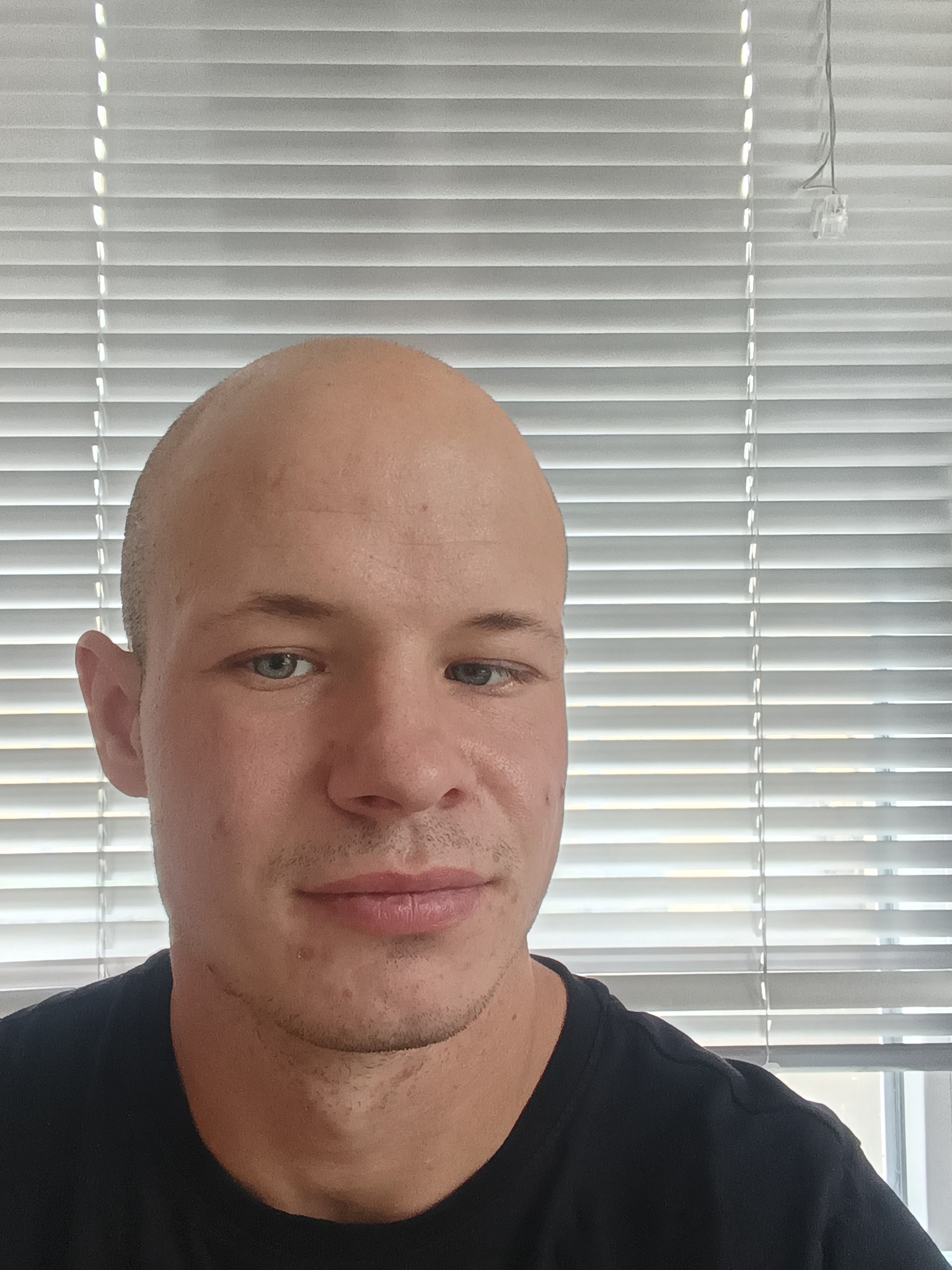 Portret mężczyzny z bliska na tle okna z żaluzjami. Widoczne detale twarzy i faktura żaluzji. Ujęcie z lekkiego dołu.