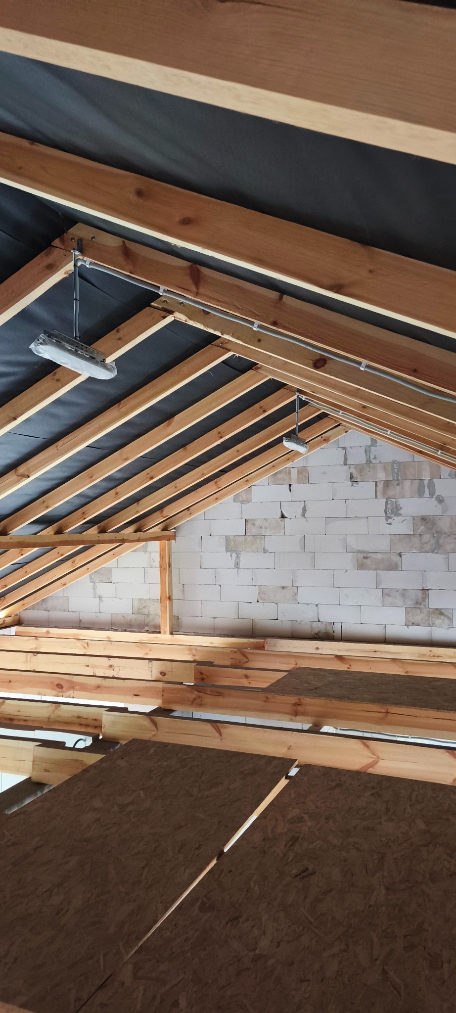 Drewniana konstrukcja dachu z izolacją i instalacją elektryczną w trakcie budowy. Widoczne elementy konstrukcyjne i przewody w peszlach.