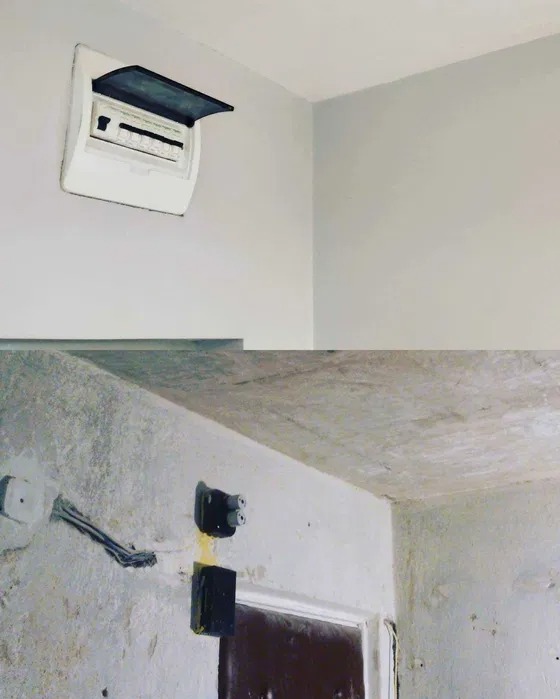 Biała skrzynka elektryczna z otwartą klapą na gładkiej ścianie, poniżej instalacja elektryczna w surowym stanie przed wykończeniem.