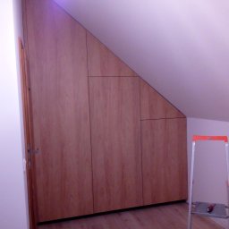 Zabudowa drewniana pod skosem na poddaszu, widoczna drabina i komoda. Realizacja szafy wnękowej na wymiar, dopasowanej do nietypowej przestrzeni.