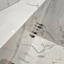 REMONT HARANT - Białe, marmurowe płytki w łazience, świeżo po ułożeniu, z widocznymi narzędziami glazurniczymi i elementami instalacji wodnej. Minimalistyczny design.