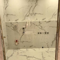 REMONT HARANT - Wykończona łazienka z białymi płytkami imitującymi marmur, widok z perspektywy wejścia, armatura zamontowana na ścianie, oświetlenie punktowe.