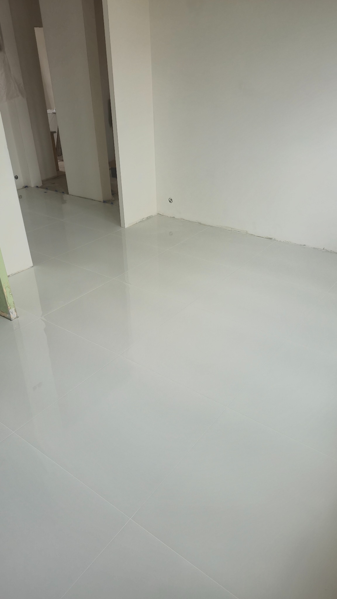 Błyszczące, jasnoszare płytki podłogowe ułożone w nowym wnętrzu w Radomsku. Widoczne fragmenty ścian i futryn drzwiowych. Minimalistyczny design.