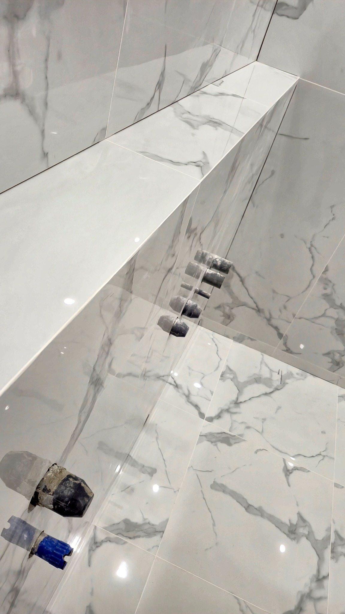 Białe, marmurowe płytki w łazience, świeżo po ułożeniu, z widocznymi narzędziami glazurniczymi i elementami instalacji wodnej. Minimalistyczny design.