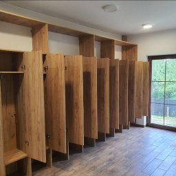 Anstol - Długa zabudowa z szaf wnękowych z drewnianymi frontami, z otwartymi i zamkniętymi przestrzeniami, w jasnym pomieszczeniu z oknem na ogród.