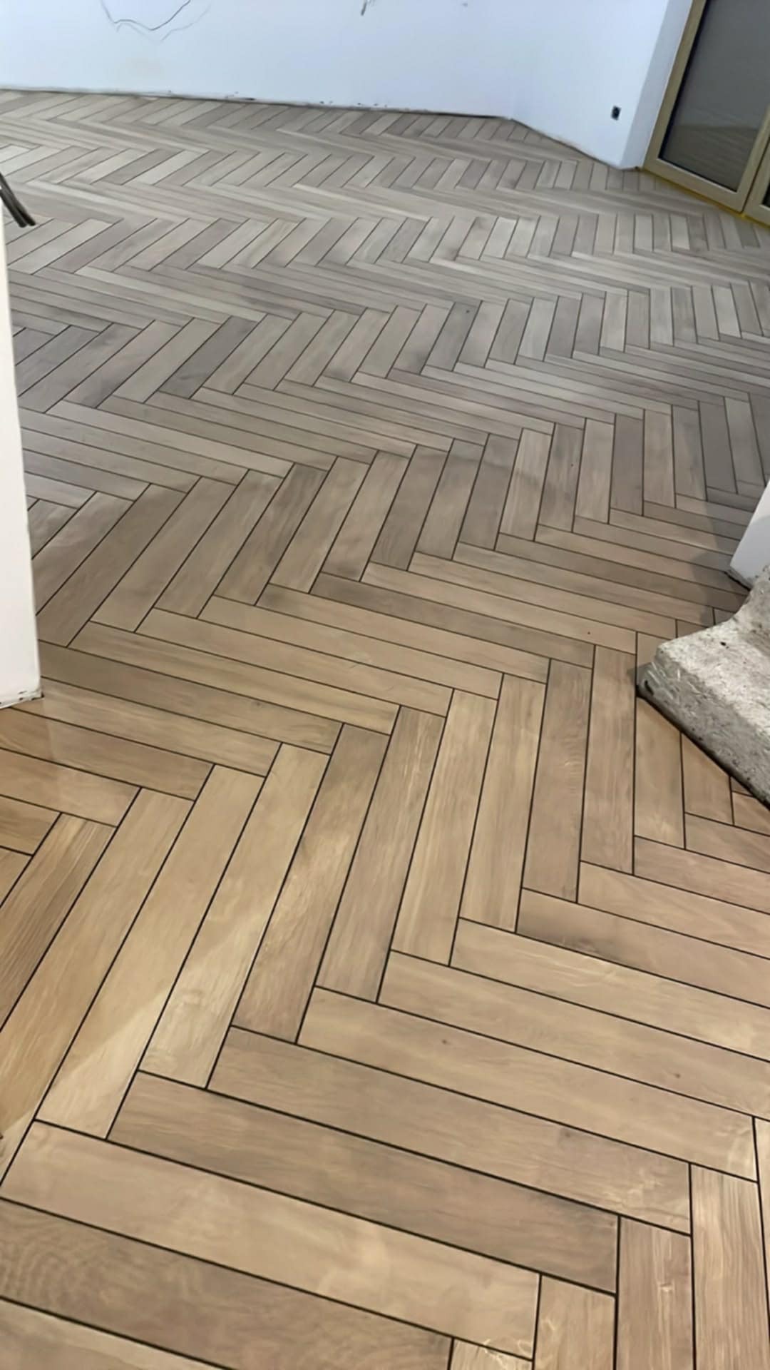 Jasne panele ułożone w jodełkę na podłodze w nowym wnętrzu. Widoczny fragment ściany i próg drzwiowy. Minimalistyczny styl wykończenia.