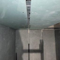 Dawid Jączkowski - Montaż płyt gipsowo-kartonowych na suficie i ścianach. Widoczne profile metalowe i szczelina między płytami. Szare ściany i sufit w trakcie wykończenia.