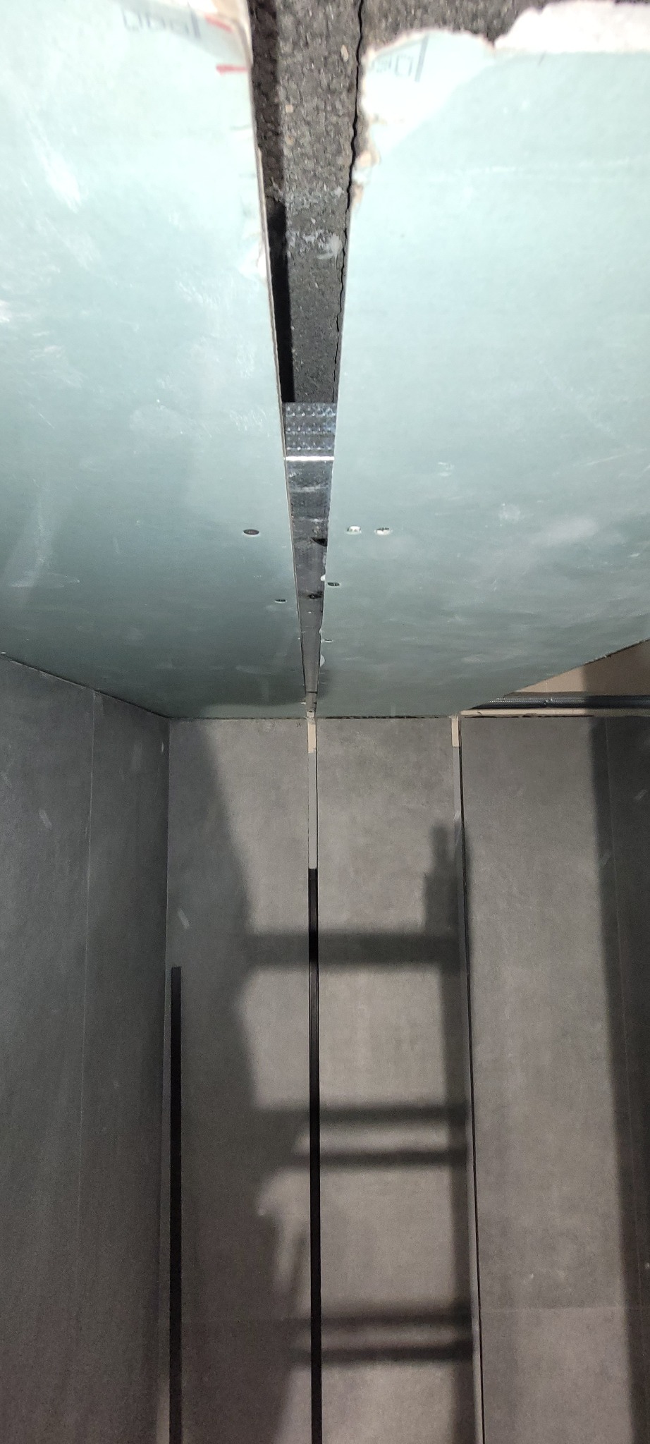 Montaż płyt gipsowo-kartonowych na suficie i ścianach. Widoczne profile metalowe i szczelina między płytami. Szare ściany i sufit w trakcie wykończenia.