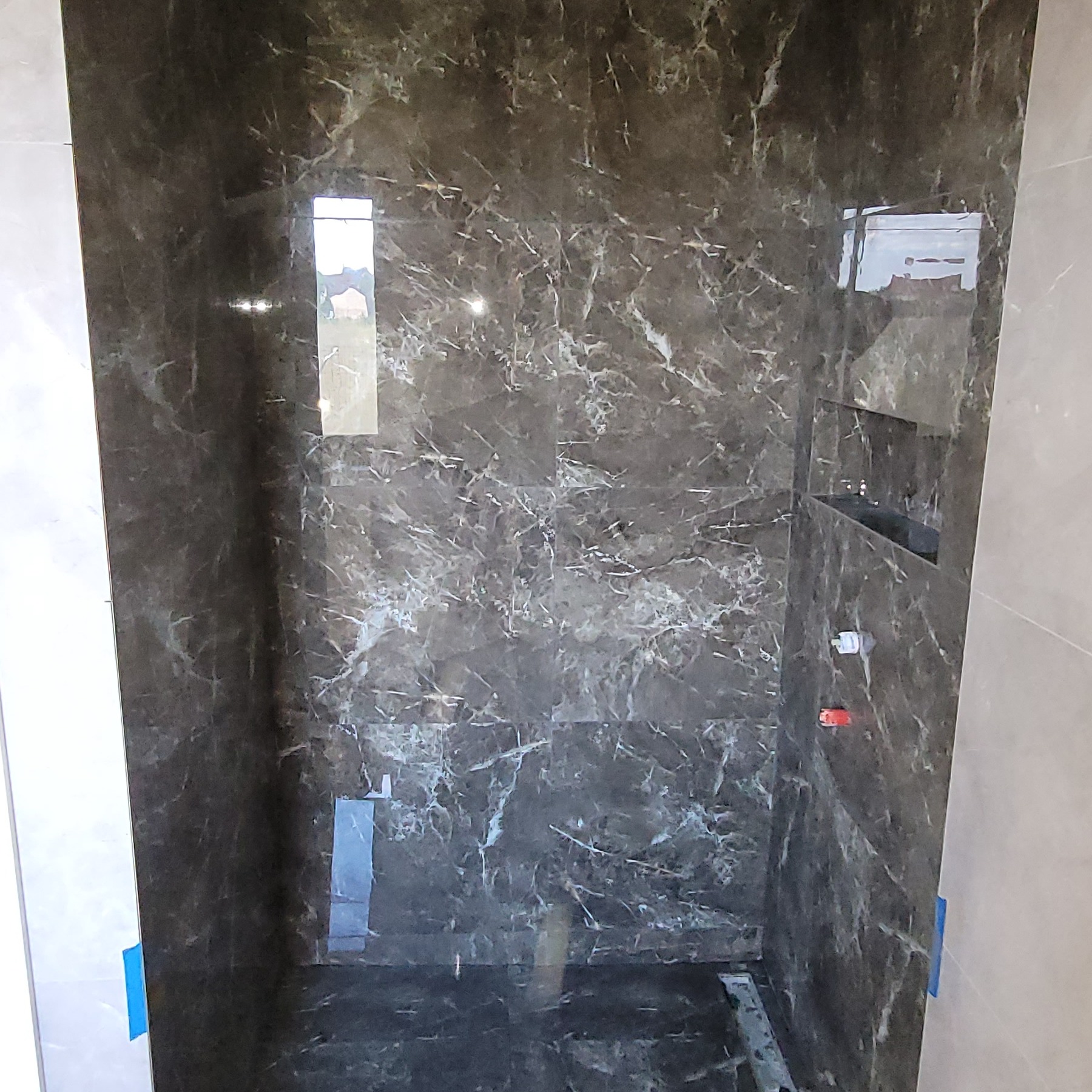 Wykończona kabina prysznicowa z ciemnymi płytkami imitującymi marmur, z widoczną wnęką na kosmetyki i elementami instalacji wodnej. Widok z góry.