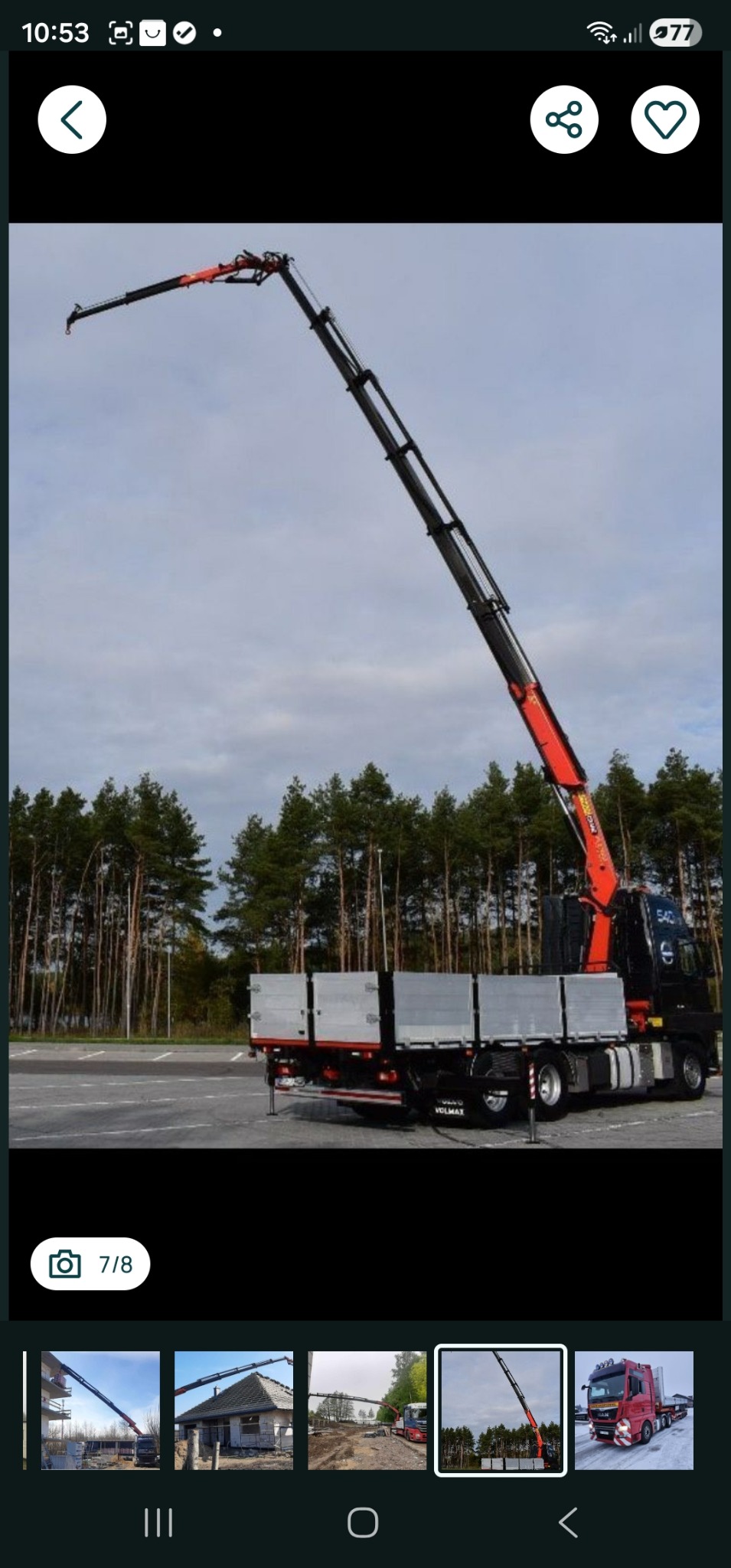 Czarny samochód ciężarowy z wysięgnikiem dźwigu, zaparkowany na parkingu, z lasem w tle. Dźwig w pozycji roboczej, gotowy do podnoszenia ładunków.