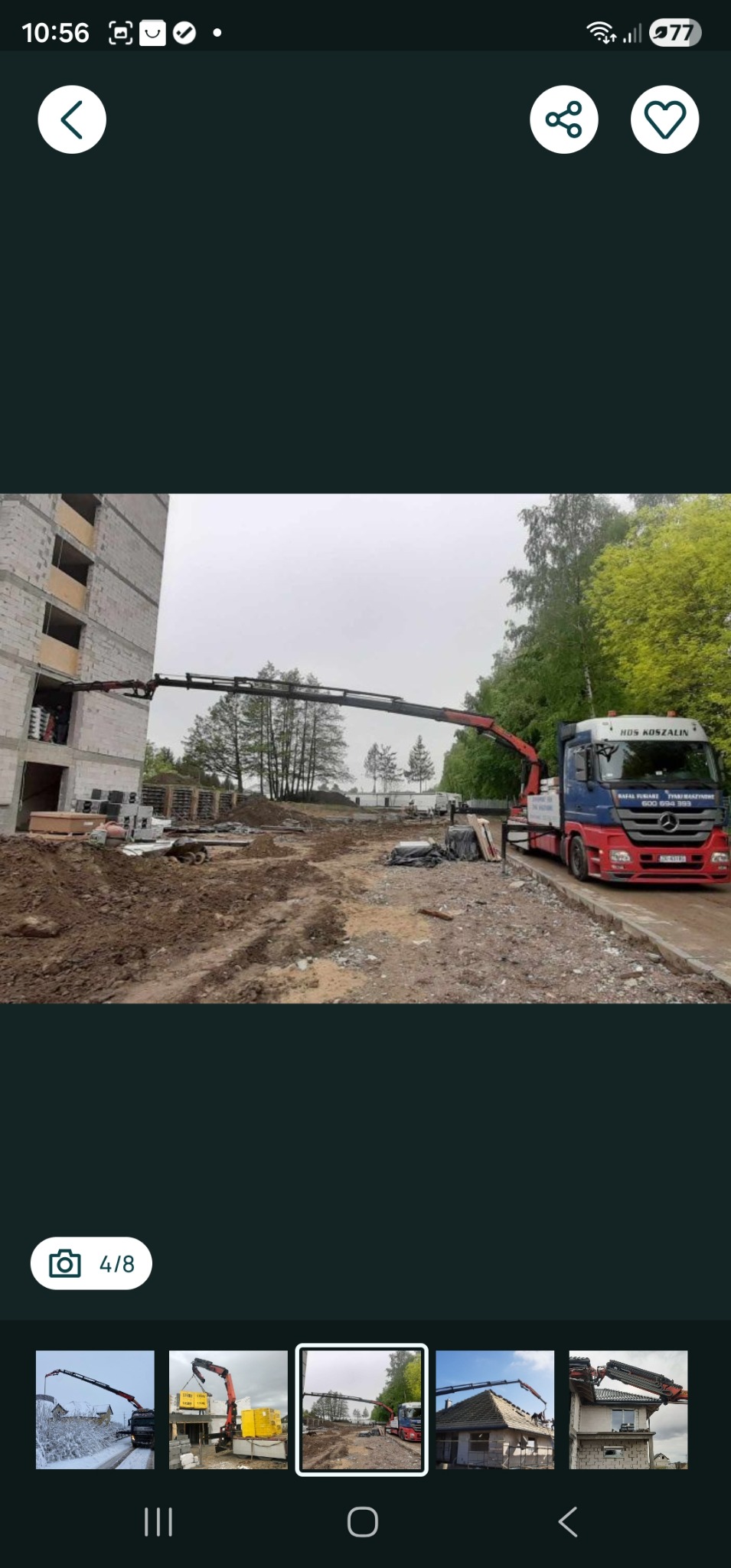 Ciężarówka z dźwigiem HDS podnosi palety z bloczkami na budowę. Widoczny budynek w stanie surowym i teren budowy. Usługa transportu ciężarowego z załadunkiem.
