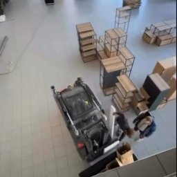 Mateusz Borkowski Trans Factory - Widok z góry na wnętrze z miniładowarką transportującą meble i kartony podczas przeprowadzki. W tle widoczny podnośnik koszowy i inne elementy wyposażenia.