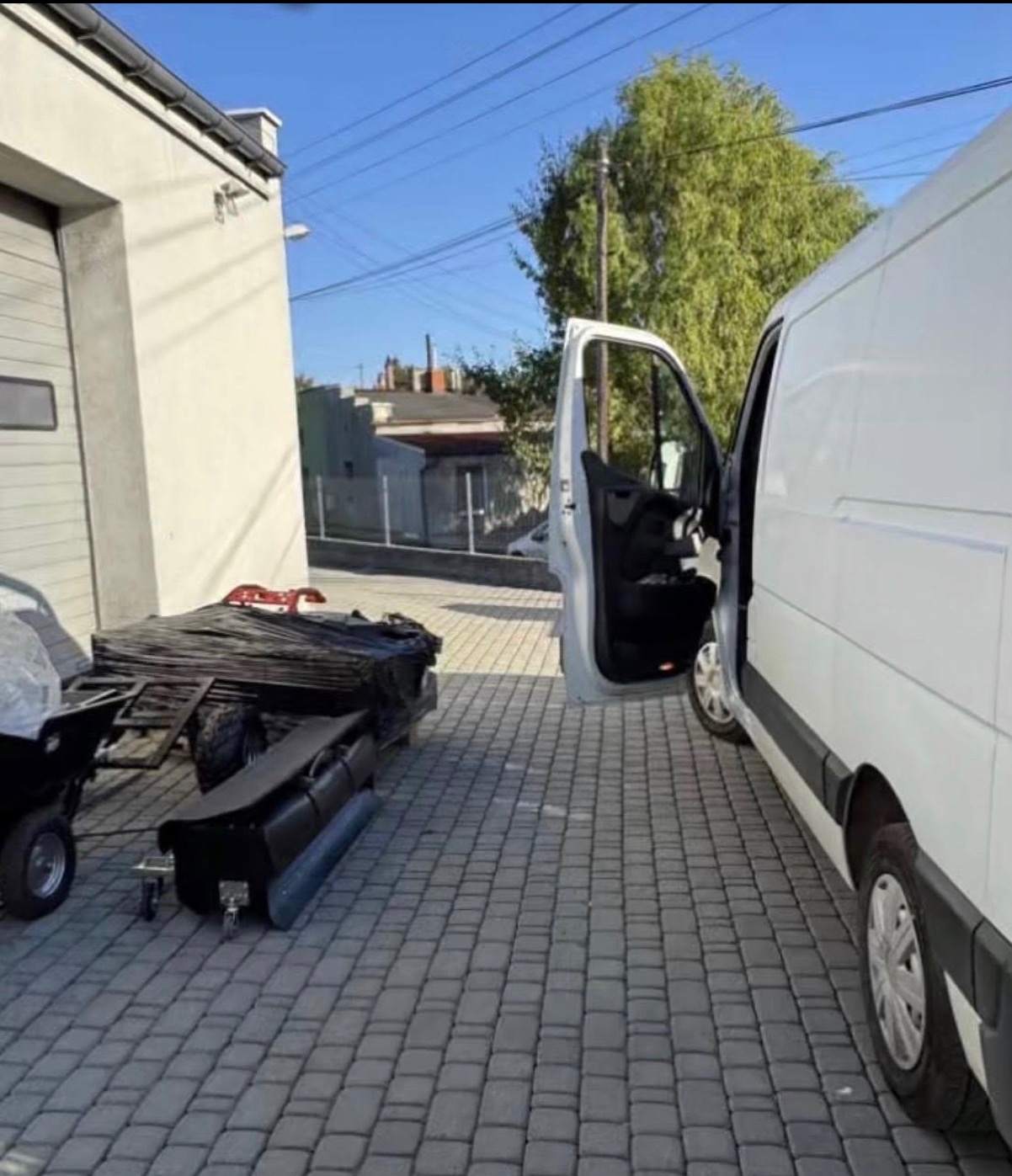 Przygotowany do załadunku wóz transportowy obok otwartego busa na brukowanym podjeździe, gotowy do przewozu ładunku w słoneczny dzień.