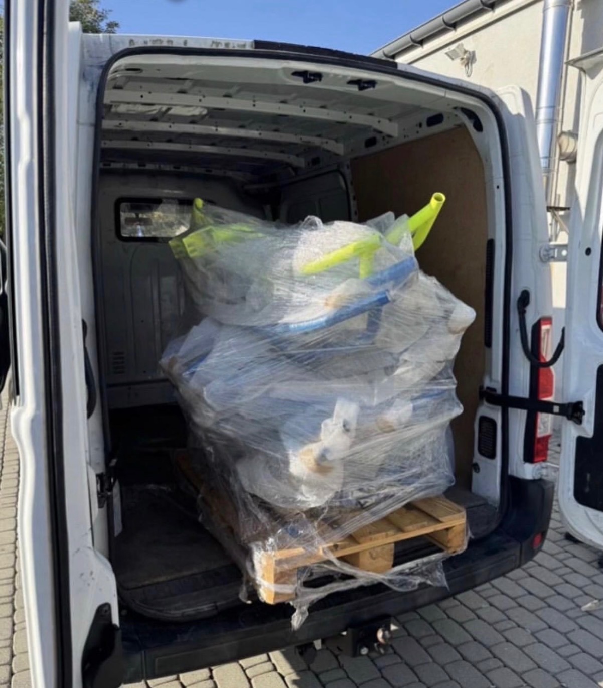 Wnętrze furgonetki z załadunkiem mebli zabezpieczonych folią stretch na palecie, gotowych do transportu. Widok z tyłu pojazdu.