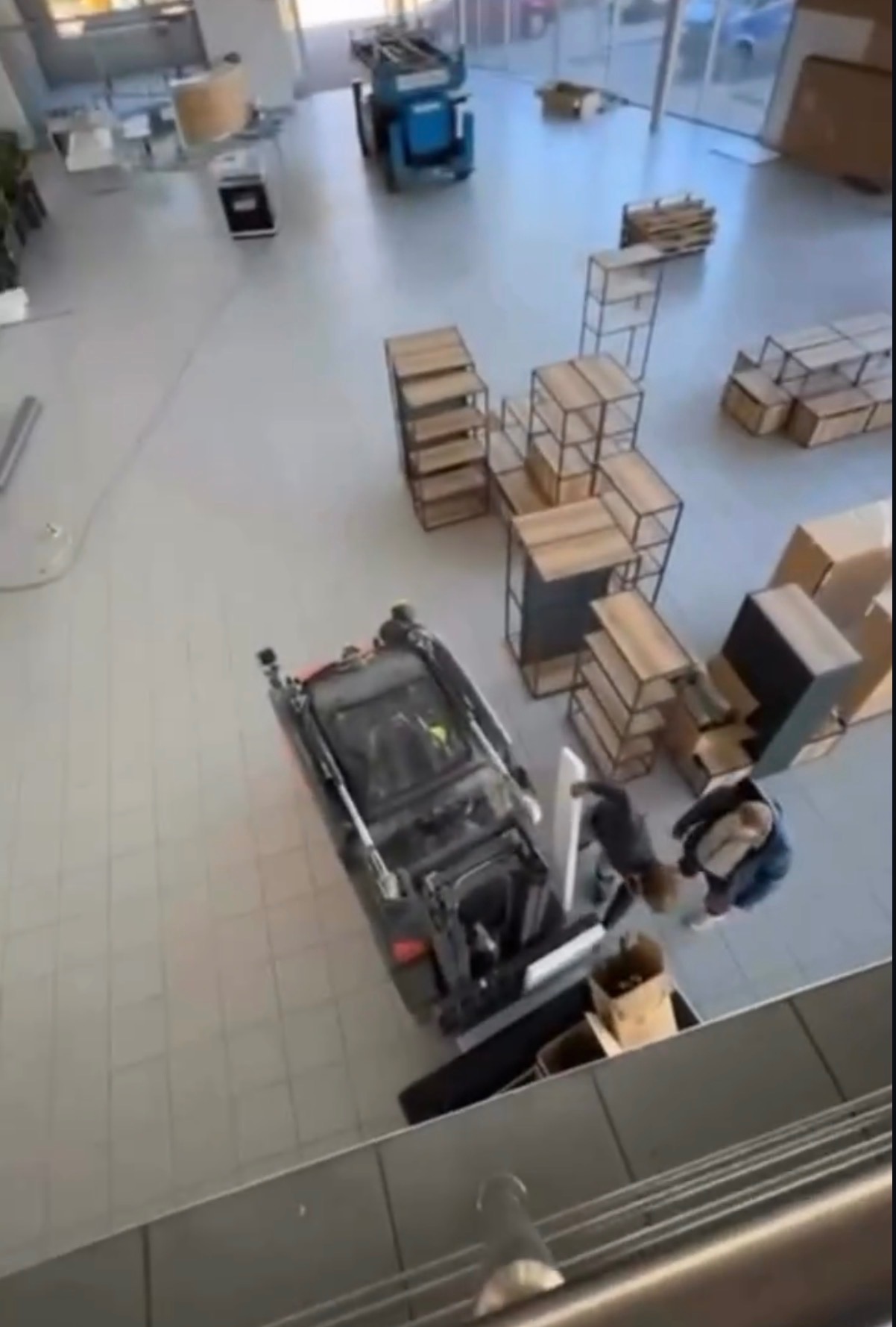 Widok z góry na wnętrze z miniładowarką transportującą meble i kartony podczas przeprowadzki. W tle widoczny podnośnik koszowy i inne elementy wyposażenia.