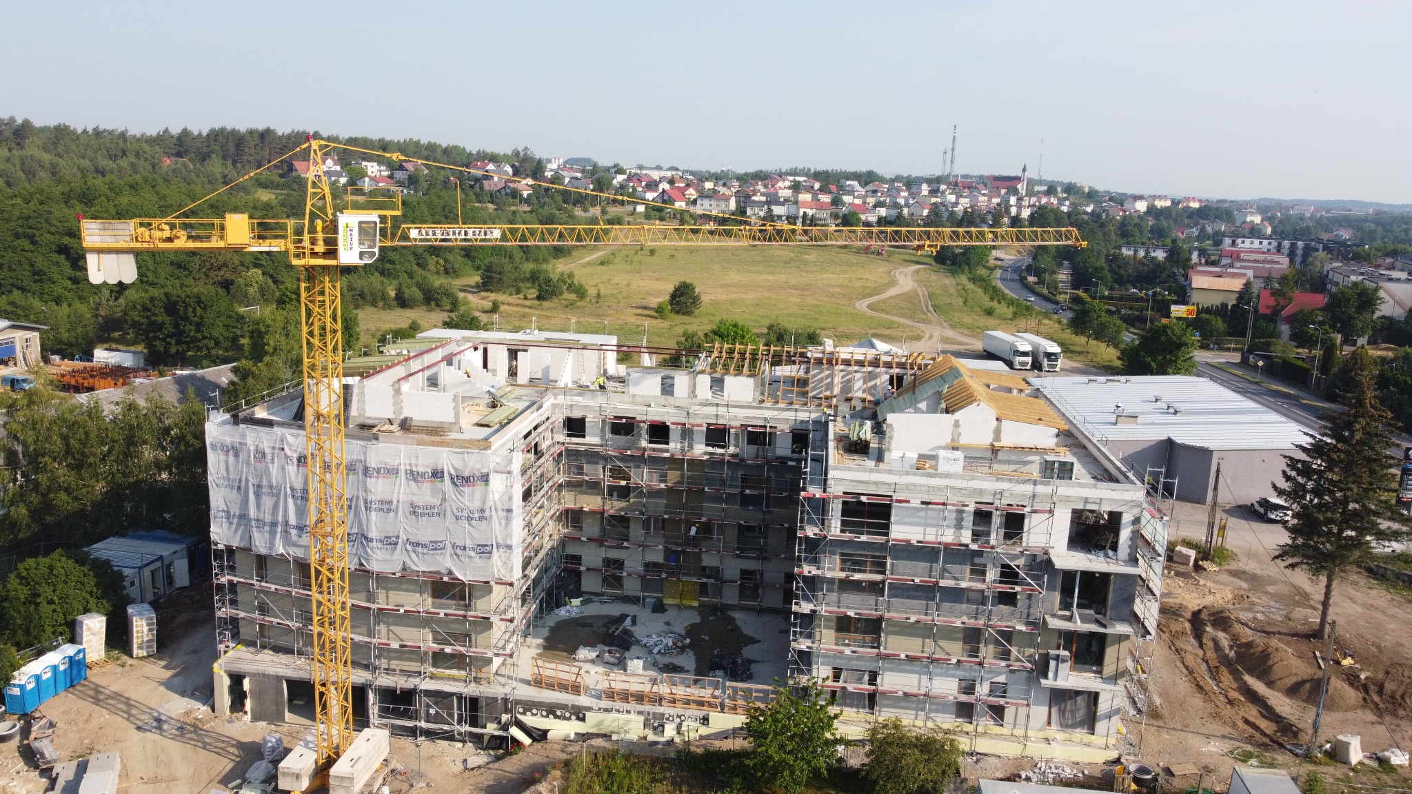 Wysoka perspektywa na budowę budynku wielorodzinnego z żelbetu, z żółtym dźwigiem wieżowym i rusztowaniami. Widok na miasto w tle.