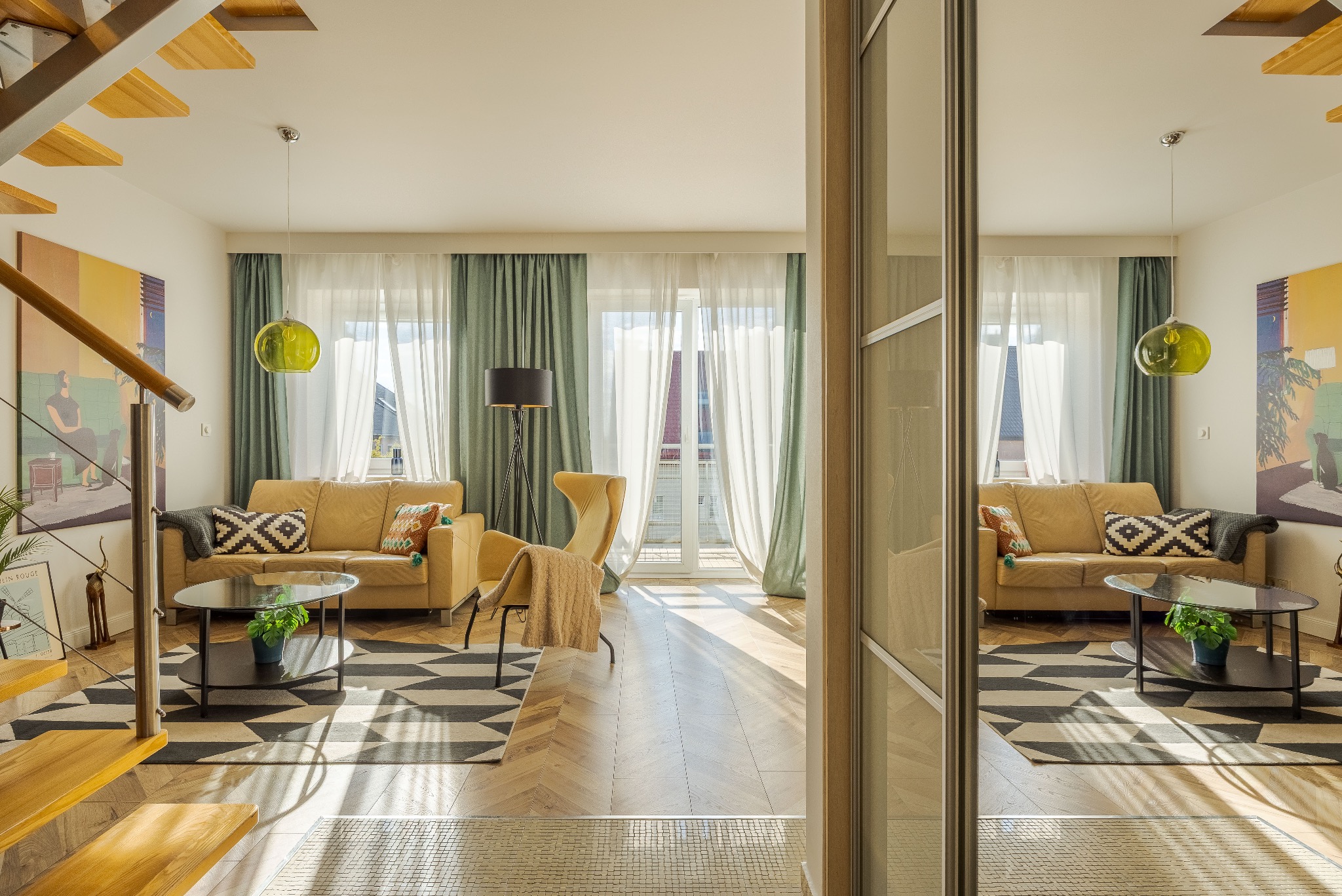 Jasne wnętrze salonu z beżową sofą, wzorzystym dywanem i schodami. Widok przez przesuwne drzwi z lustrem, odbijające identyczny układ pomieszczenia.