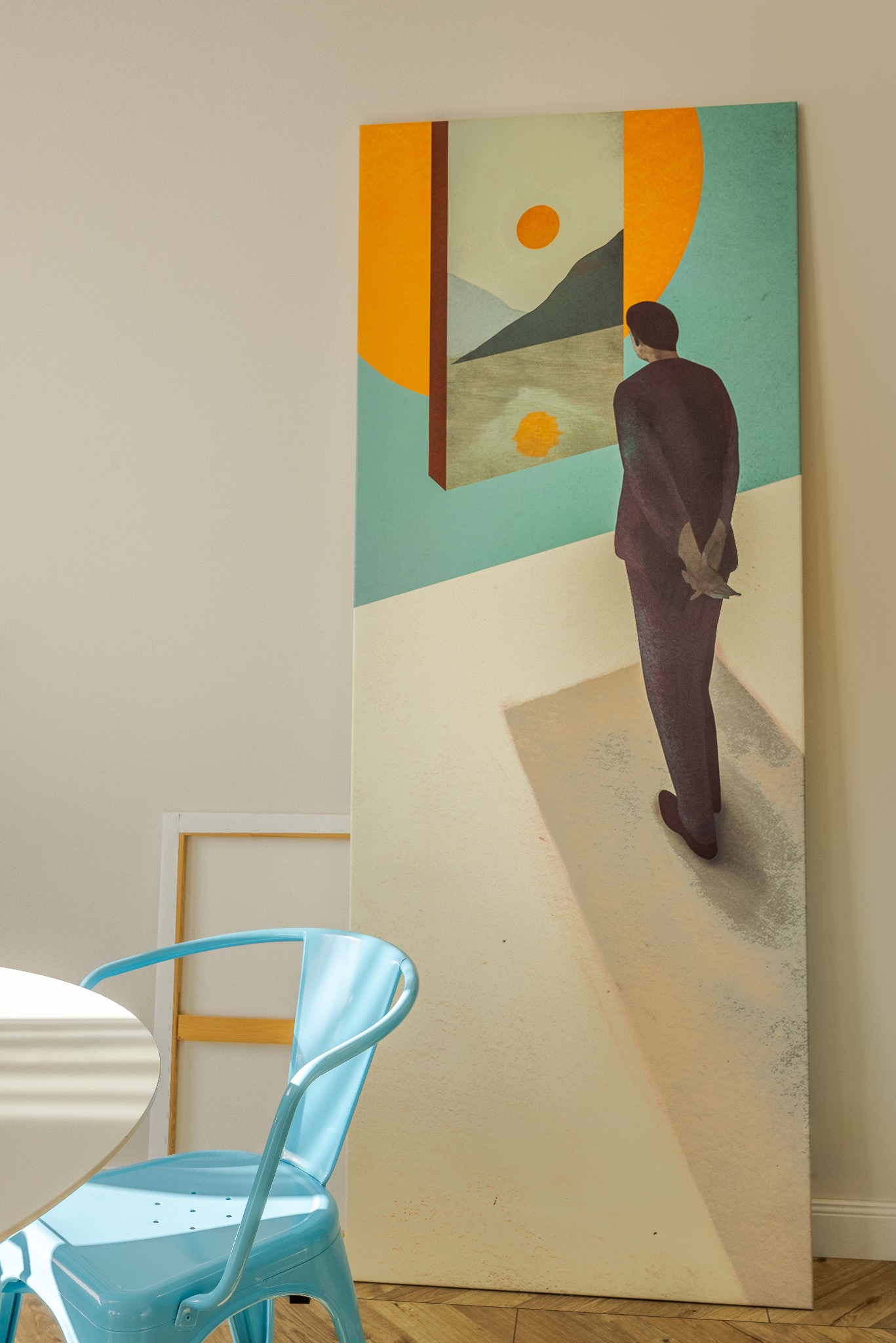 Wysoki obraz w jasnym wnętrzu: mężczyzna w ciemnym garniturze stoi tyłem, patrząc na abstrakcyjny pejzaż z geometrycznymi elementami. Obok błękitne krzesło i fragment stołu.