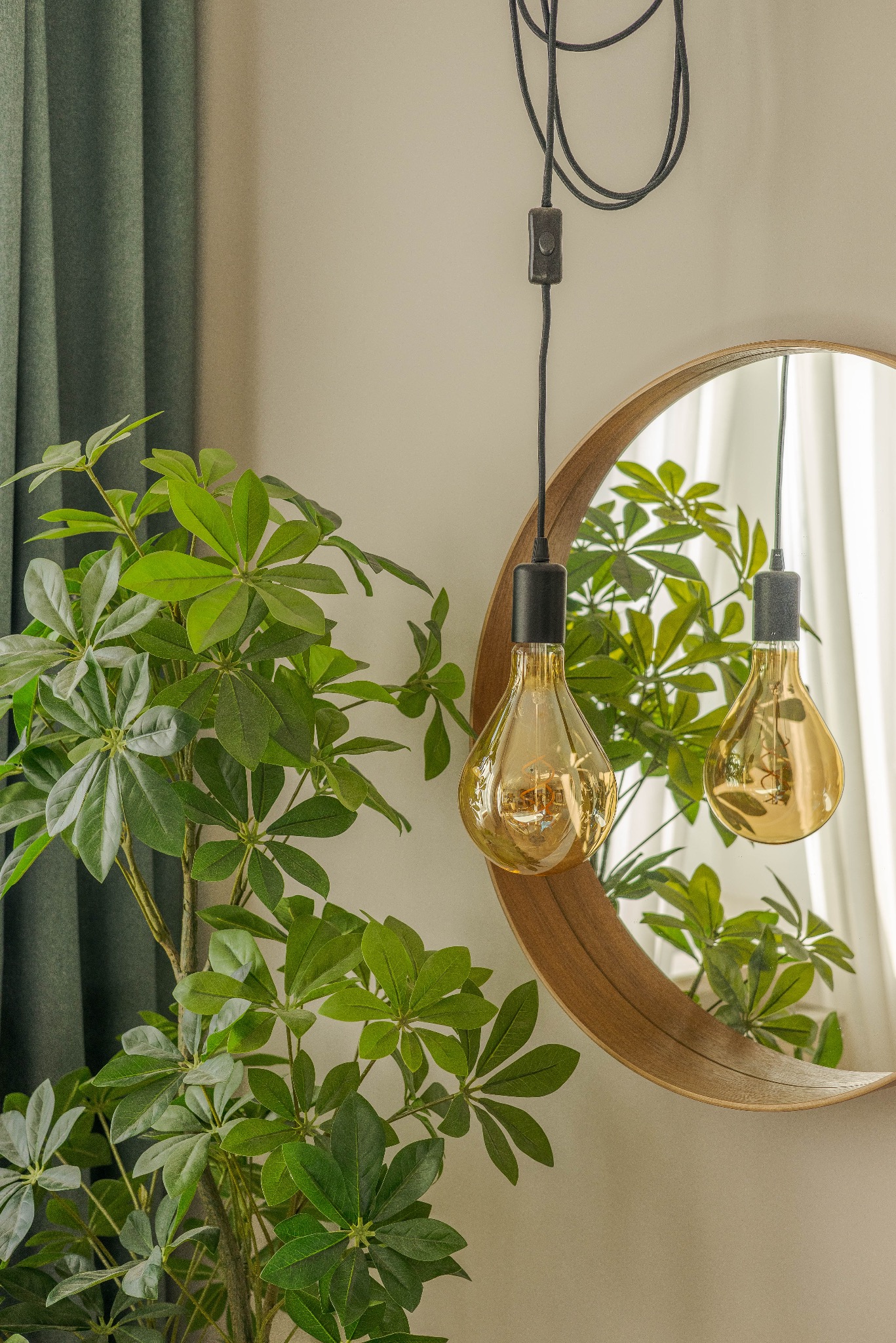 Stylowe wnętrze z okrągłym lustrem, rośliną doniczkową i wiszącą lampą z żarówką Edison. Element dekoracyjny wnętrza, oświetlenie i zieleń w harmonii.