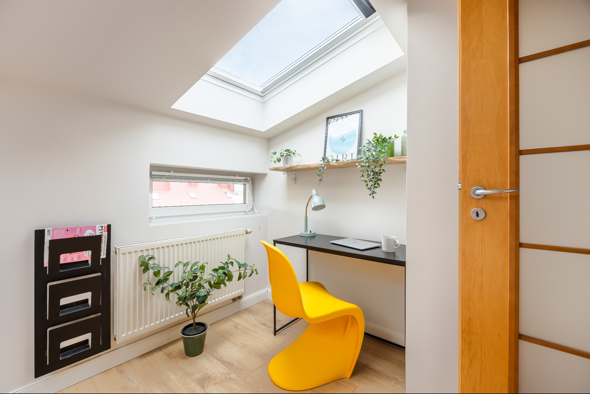 Jasne biuro w Warszawie z oknem dachowym, żółtym krzesłem i czarnym biurkiem. Minimalistyczny design, roślina doniczkowa i półka z dekoracjami.
