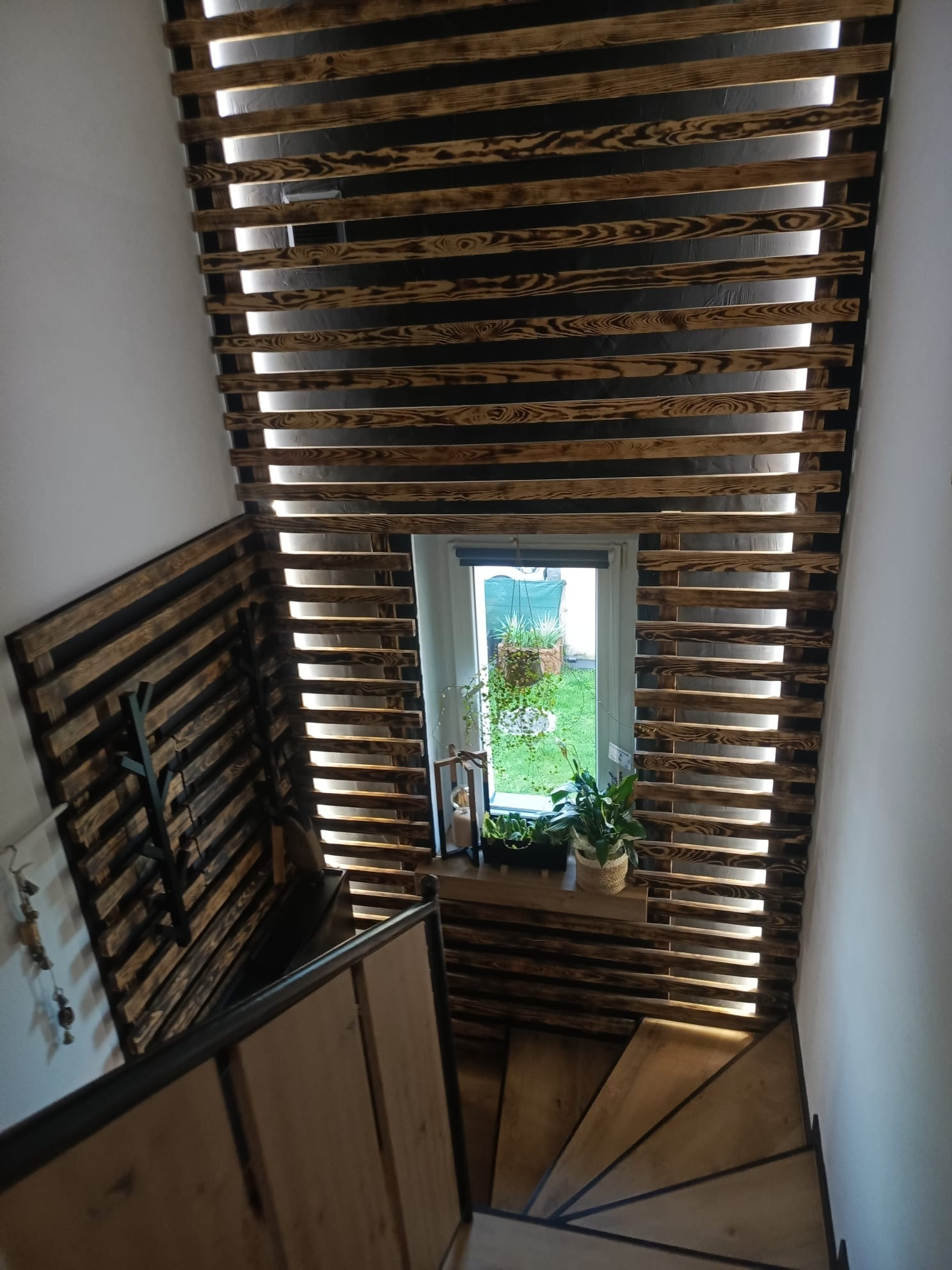 Drewniana ażurowa ścianka działowa z palet przy schodach, z oknem w tle. Widok z góry, ciepłe oświetlenie. Element wystroju wnętrza.