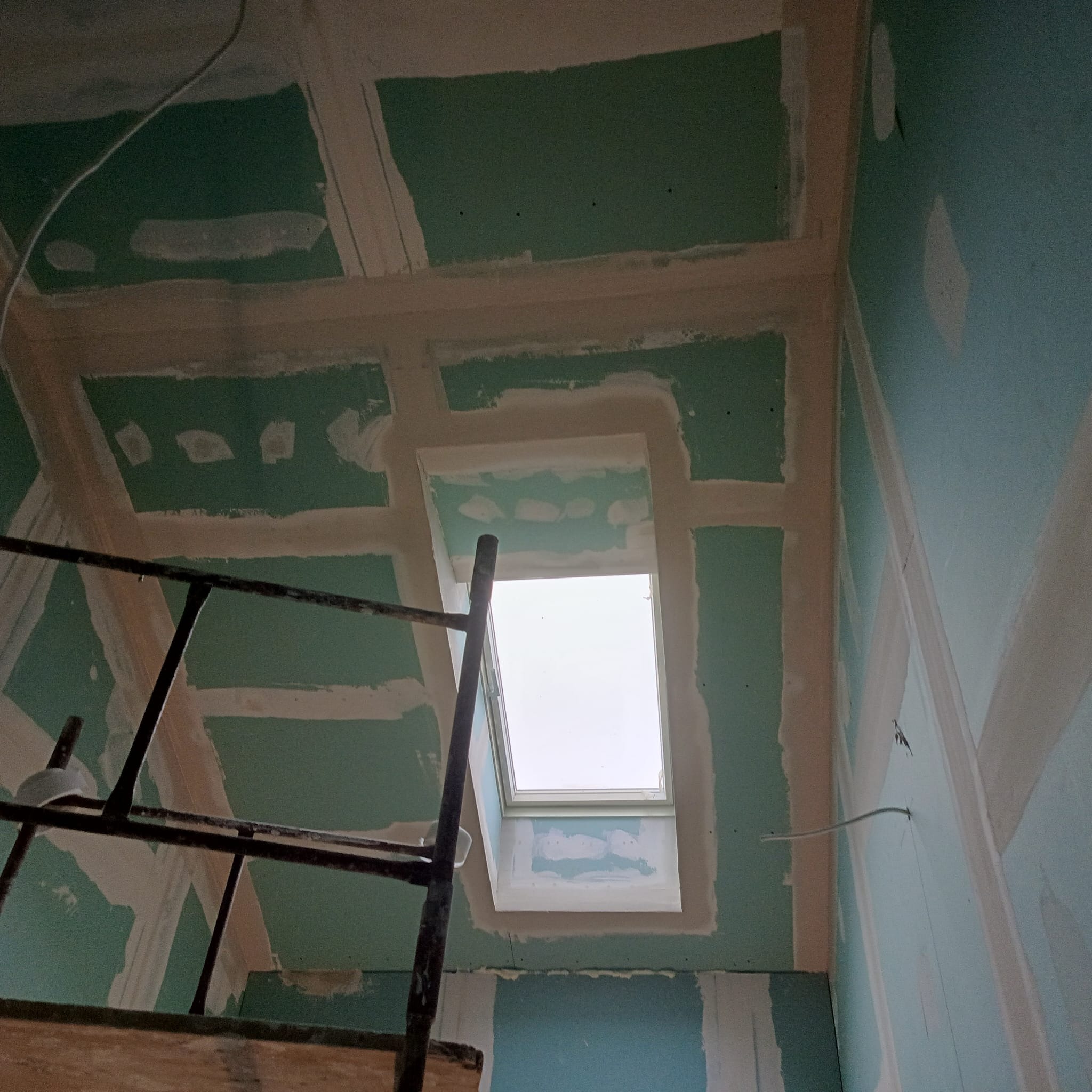 Sufit z płyt gipsowo-kartonowych w trakcie szpachlowania, widok z dołu, rusztowanie w lewym dolnym rogu, okno dachowe w centrum kadru.