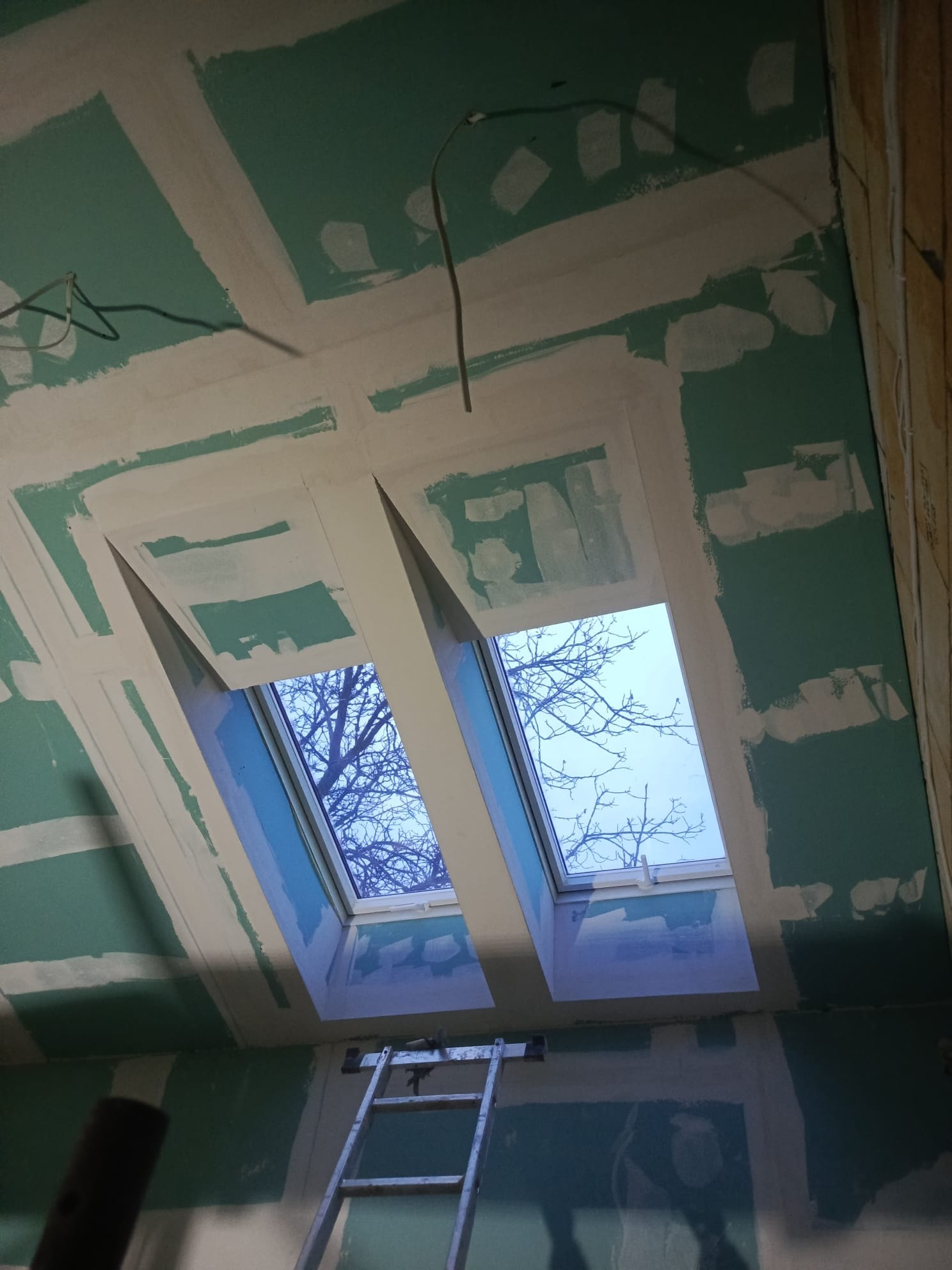 Montaż płyt G-K na poddaszu w Bytomiu. Widoczne okna dachowe i drabina. Ściany przygotowane do szpachlowania, z widocznymi łączeniami płyt. Prace wykończeniowe.