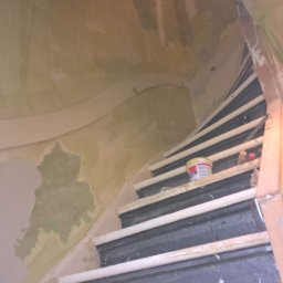 Rob-Kop - Klatka schodowa w trakcie szpachlowania ścian, widoczne ślady po gładzi, puszka z farbą na schodach. Ujęcie z dołu, spiralne schody.