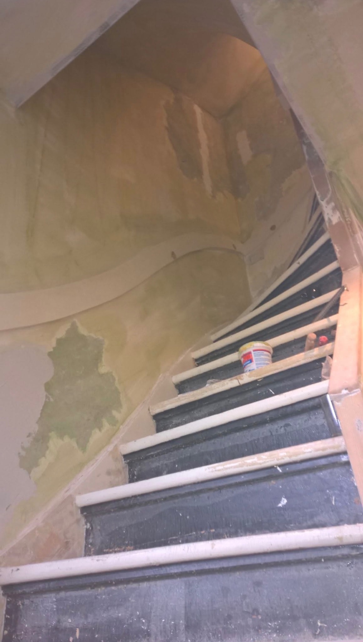 Klatka schodowa w trakcie szpachlowania ścian, widoczne ślady po gładzi, puszka z farbą na schodach. Ujęcie z dołu, spiralne schody.