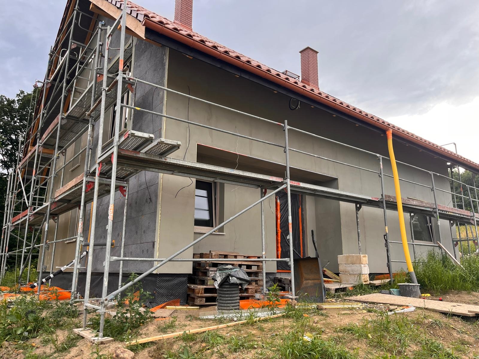 Dom w Wałbrzychu w trakcie ocieplania, widoczne rusztowania i warstwy izolacyjne na elewacji. Prace budowlane w toku, z bliska.
