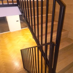 Usługi ślusarskie Paweł Drzazga - Nowoczesne schody drewniane z czarną, metalową balustradą. Widok z góry na parkiet w jodełkę i minimalistyczne wykończenie wnętrza.
