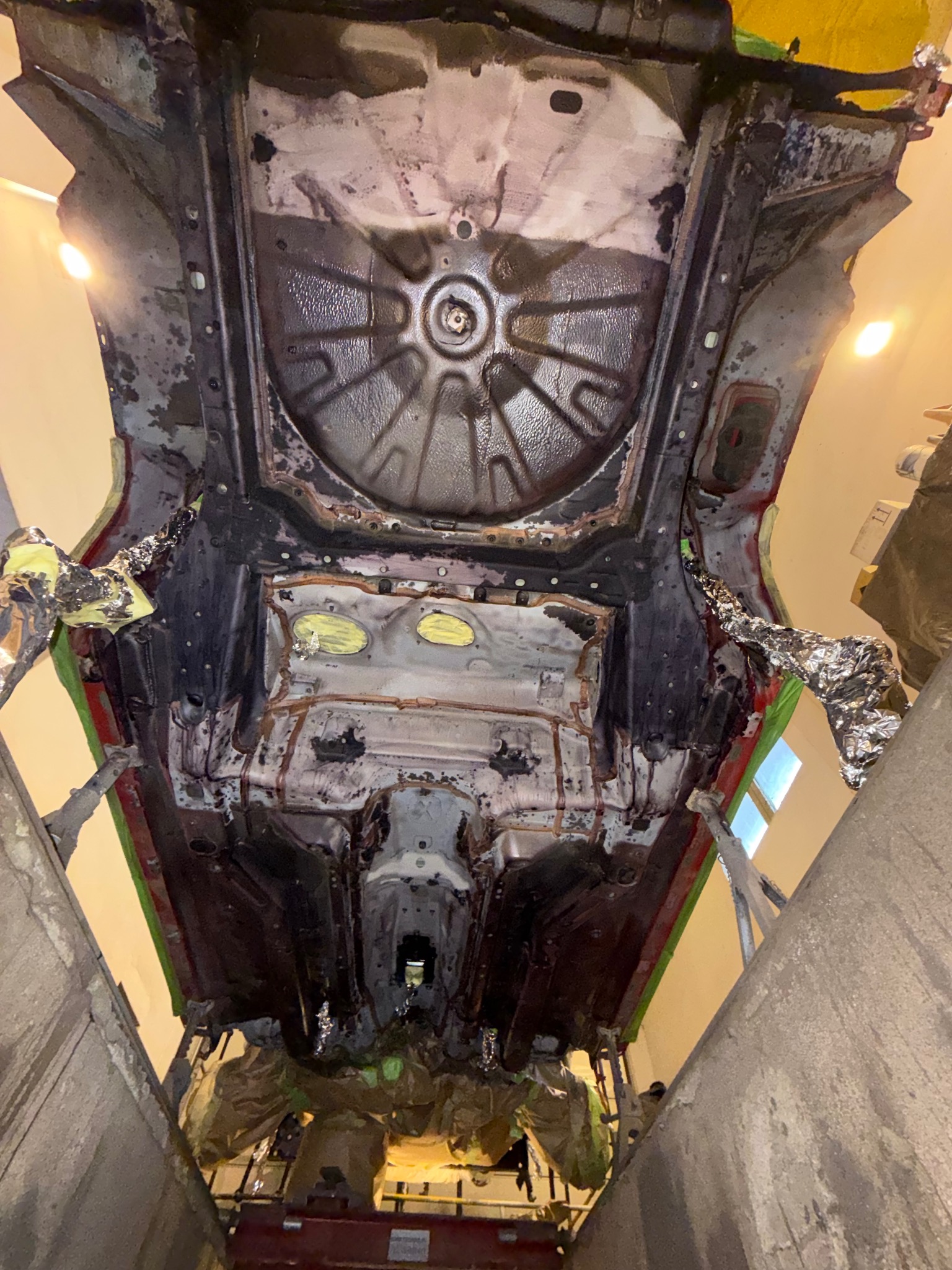 Podwozie samochodu na podnośniku w trakcie prac konserwacyjnych. Widoczne elementy zabezpieczone folią i taśmą, przygotowane do dalszej obróbki.