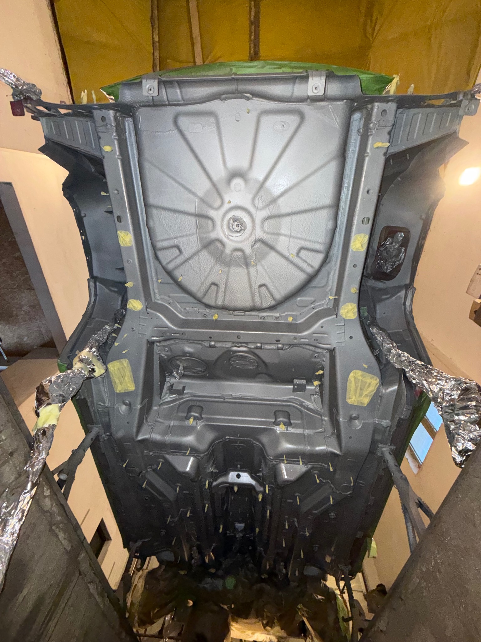 Podwozie samochodu po konserwacji antykorozyjnej, zabezpieczone folią i taśmą, widoczne detale konstrukcyjne i świeża powłoka ochronna w warsztacie.