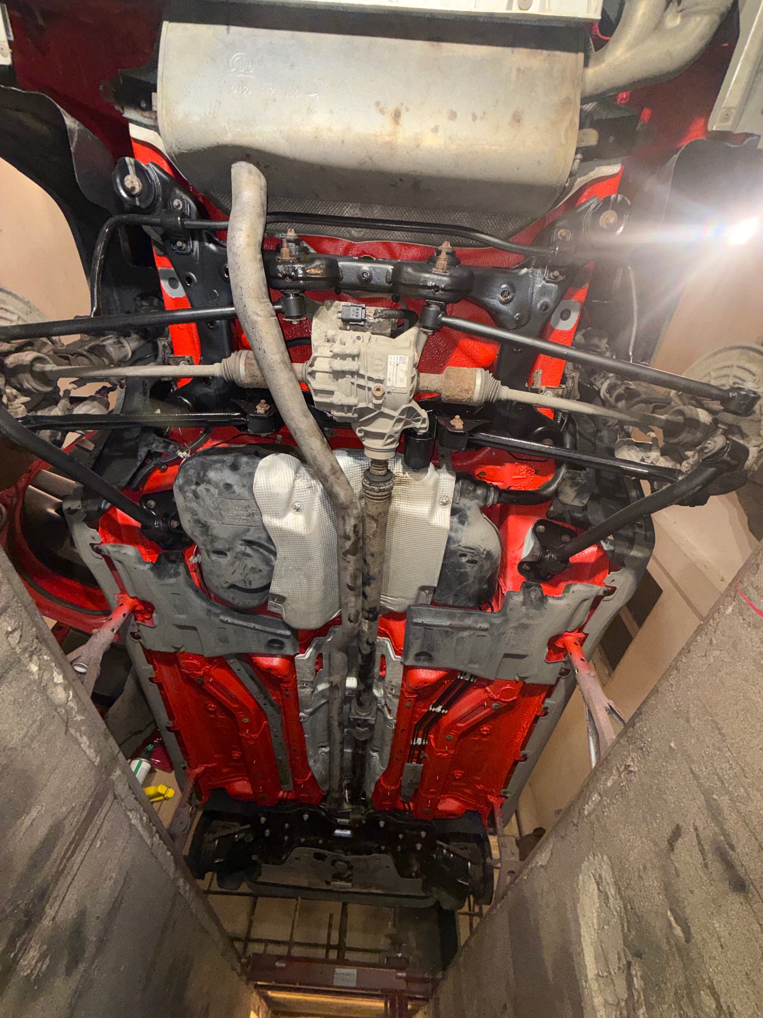 Czerwone podwozie auta po konserwacji antykorozyjnej, widoczne z kanału. Elementy zawieszenia i układu wydechowego. Jasne oświetlenie w tle.