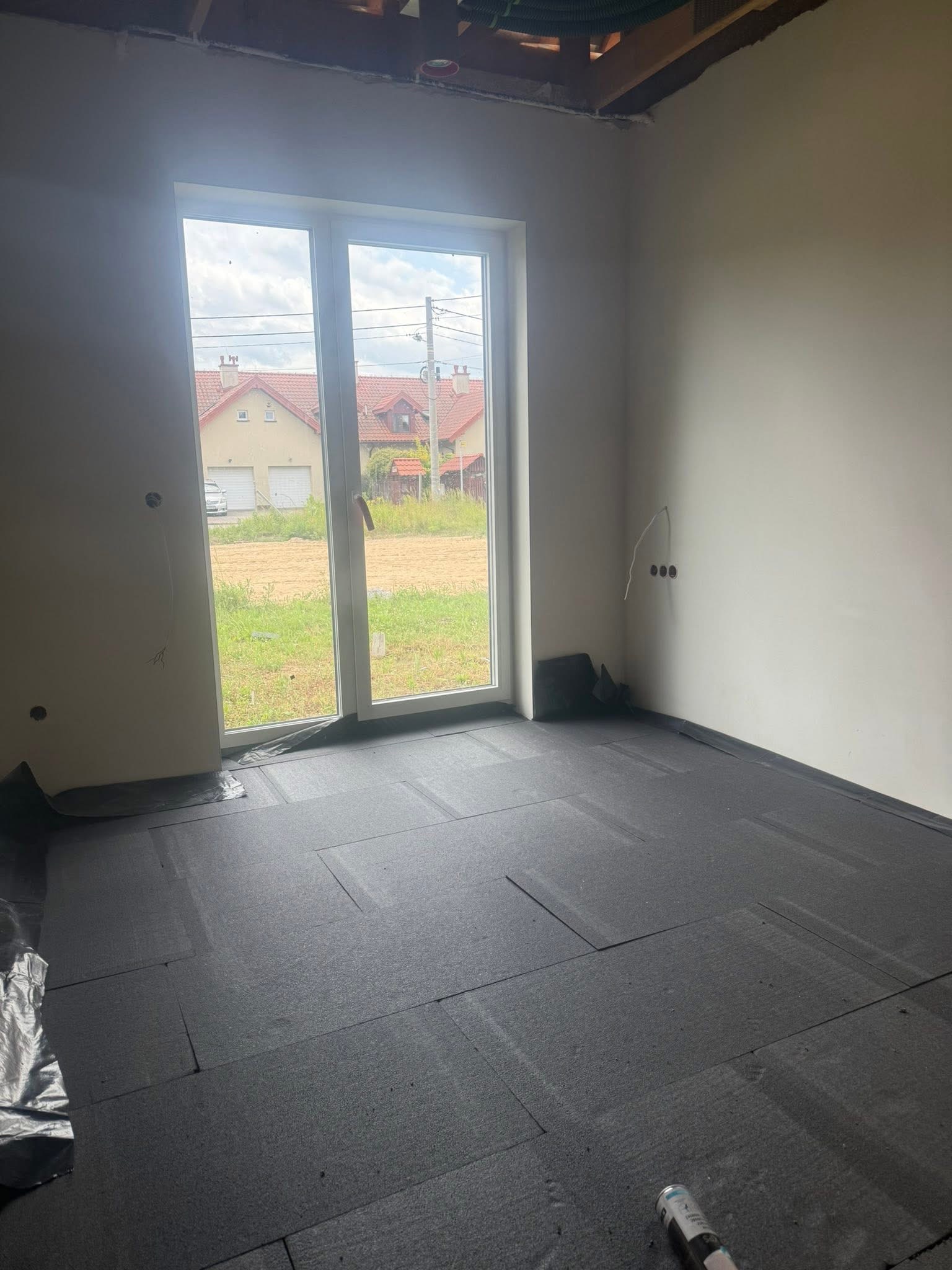 Przygotowanie podłoża pod wylewkę w Zakliczynie. Rozłożone płyty izolacyjne na podłodze, widoczne okno i surowy stan ścian. Etap prac przed wylaniem posadzki.