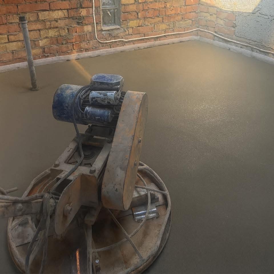 Zacieraczka mechaniczna na świeżo wylanej, gładkiej powierzchni. Ceglana ściana w tle. Widok z góry, oświetlenie naturalne.