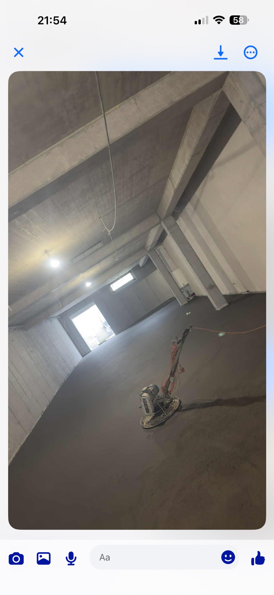 Wnętrze w trakcie prac posadzkarskich: zacieraczka mechaniczna na świeżo wylanej, szarej posadzce w surowym pomieszczeniu z widocznymi elementami konstrukcyjnymi.