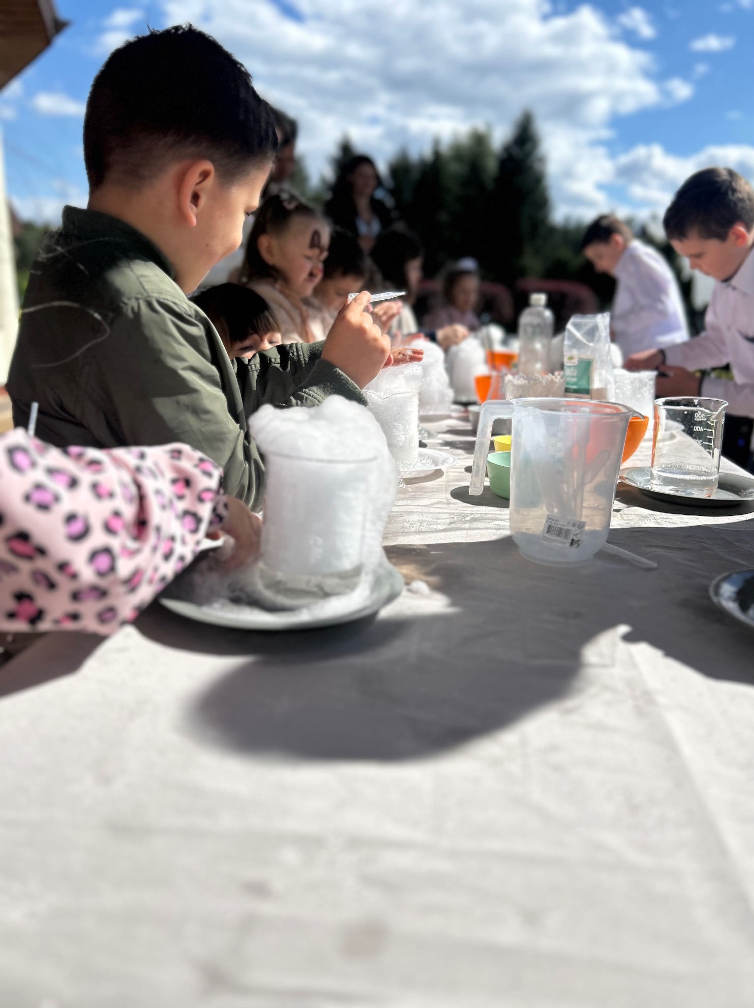 Dzieci eksperymentują z suchym lodem podczas pokazu naukowego na świeżym powietrzu, zlewki i naczynia na stole, edukacyjna zabawa.
