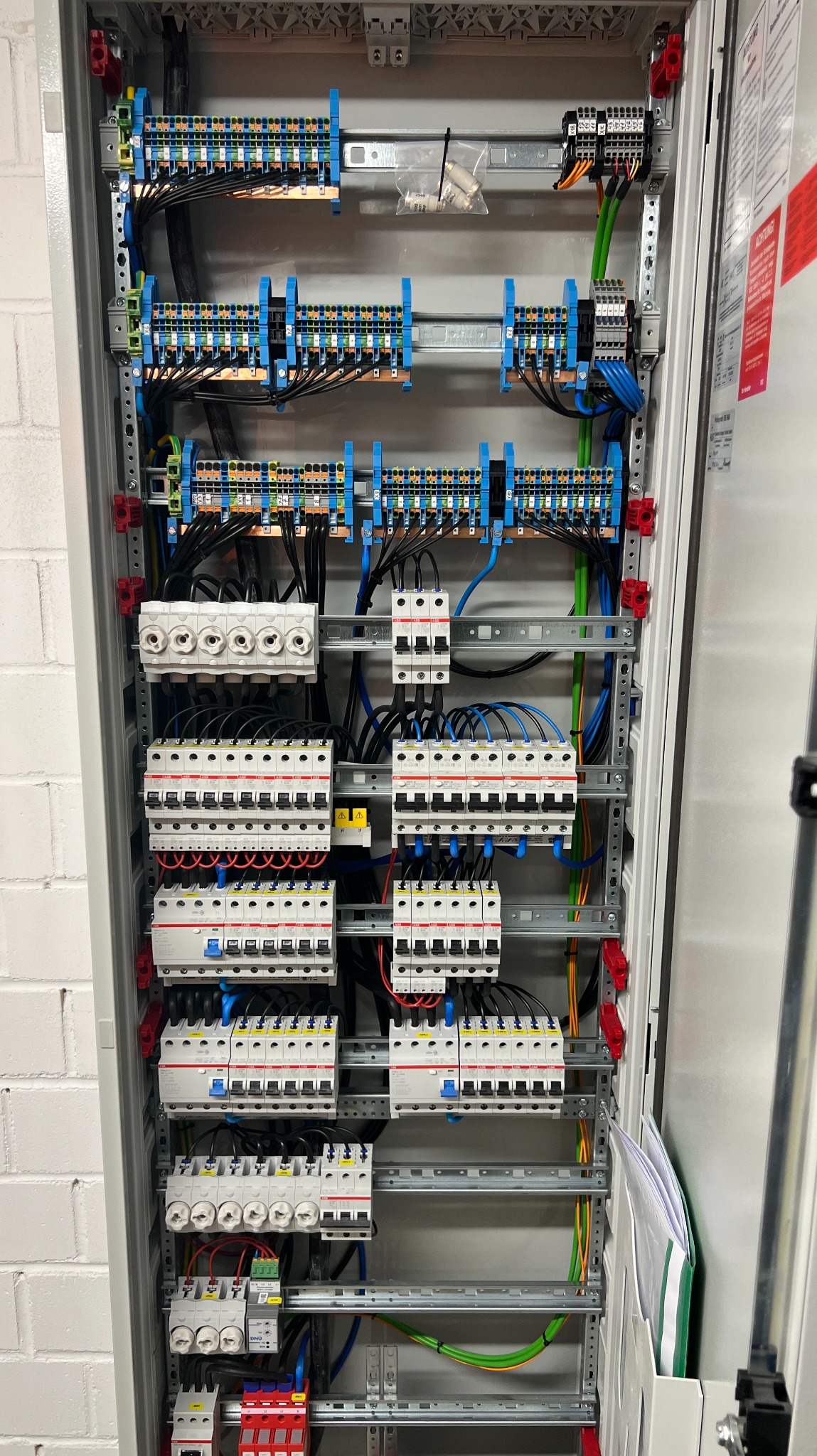 Rozdzielnia elektryczna z bezpiecznikami, listwami zaciskowymi i okablowaniem wewnątrz szafy. Widoczne elementy instalacji elektrycznej w szarej obudowie.