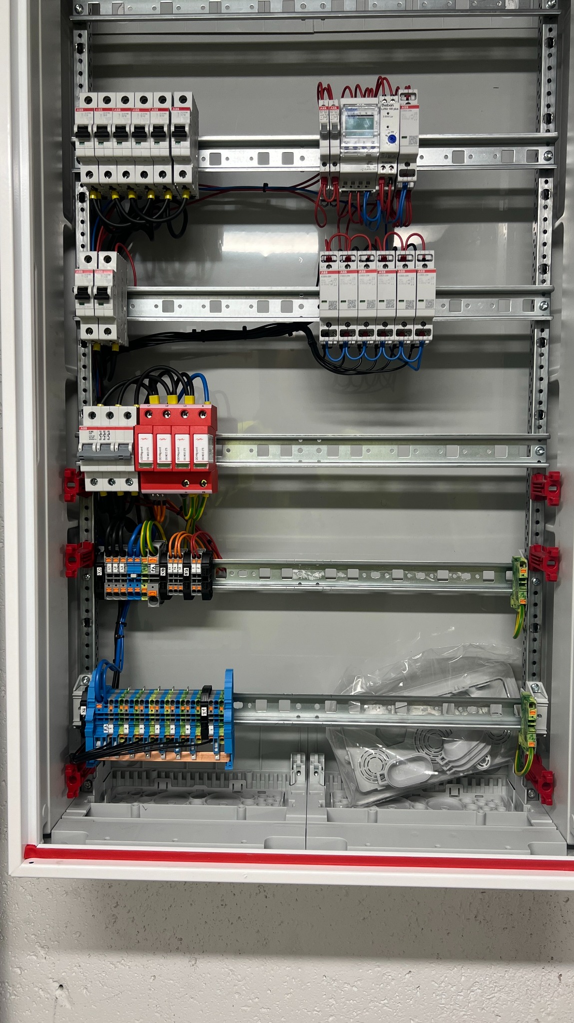 Rozdzielnica elektryczna z zabezpieczeniami, bezpiecznikami i przewodami wewnątrz metalowej obudowy. Widoczne elementy instalacji elektrycznej w szarej skrzynce.