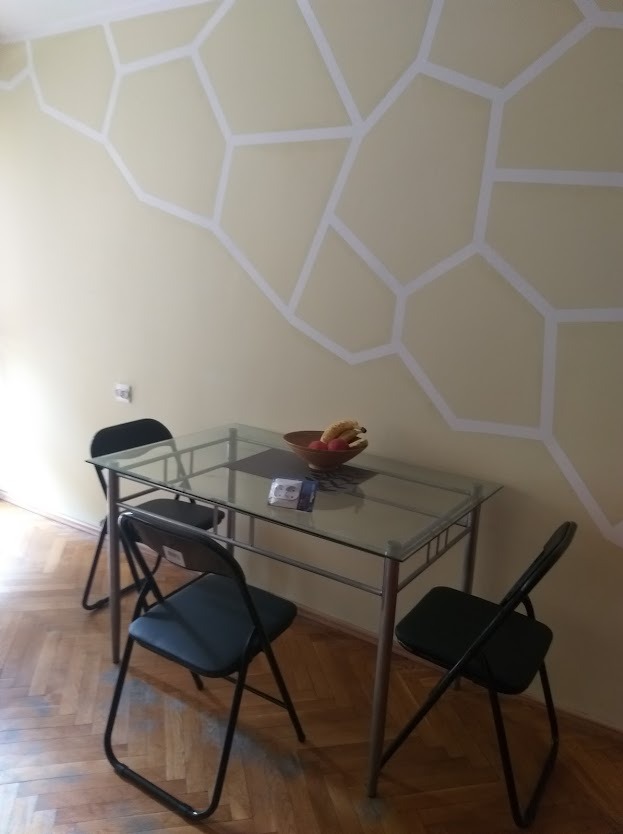 Jasna ściana z geometrycznym wzorem w stylu plastra miodu, szklany stół z owocami i krzesłami na parkiecie. Dekoracja wnętrza z bliska.