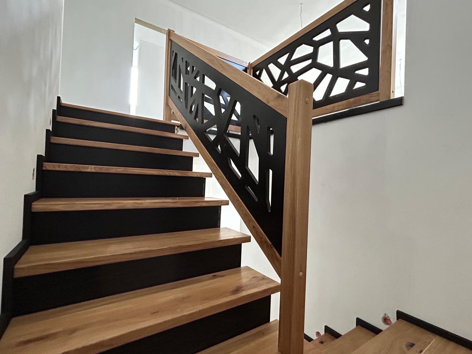 Nowoczesne schody drewniane z czarnymi podstopnicami i ażurową balustradą, widok z dołu, jasne wnętrze.