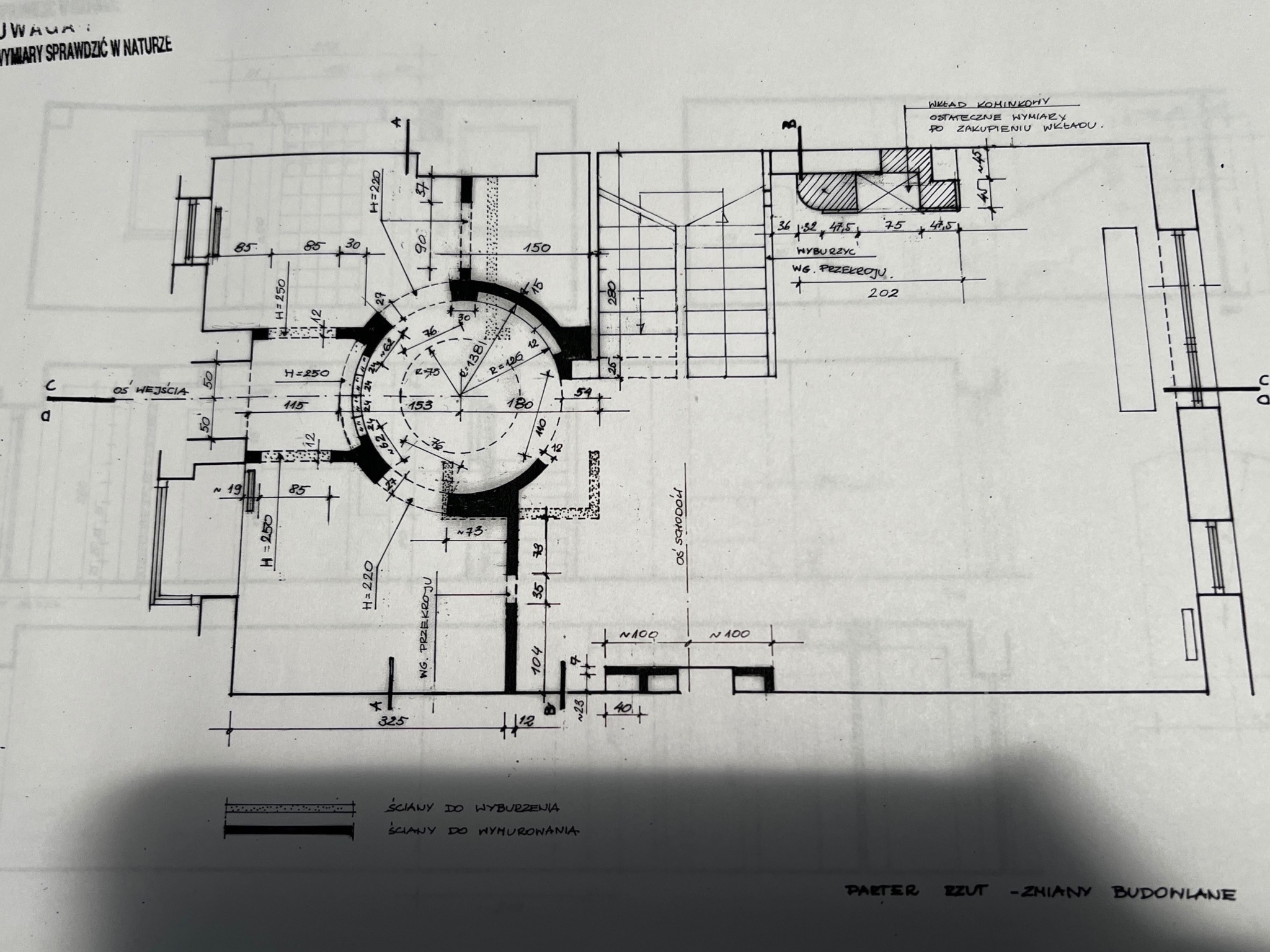 Ręcznie rysowany plan architektoniczny parteru z naniesionymi zmianami budowlanymi, wymiarami i oznaczeniami ścian do wyburzenia i wymurowania. Widoczne detale schodów i kominka.