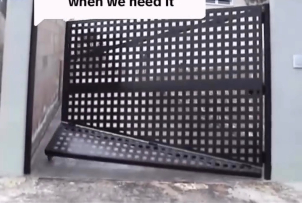 Czarna, metalowa brama z kwadratową siatką, częściowo otwarta, z widocznym fragmentem muru i chodnika. Brama sprawia wrażenie solidnej i nowoczesnej.