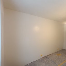 Gnat Bud - Świeżo pomalowane ściany w jasnym odcieniu, widoczne żółte zabezpieczenia podłogi i listew przypodłogowych. Minimalistyczne wnętrze po malowaniu.