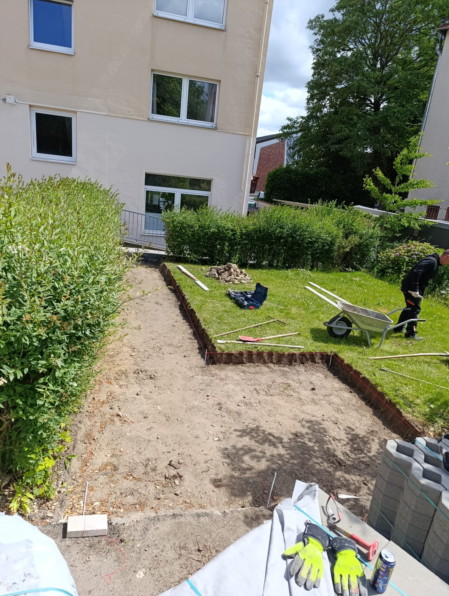 Przygotowanie terenu pod ścieżkę w ogrodzie: wytyczone granice, usunięta darń, widoczne narzędzia i materiały budowlane. Prace ziemne w toku, słoneczny dzień.