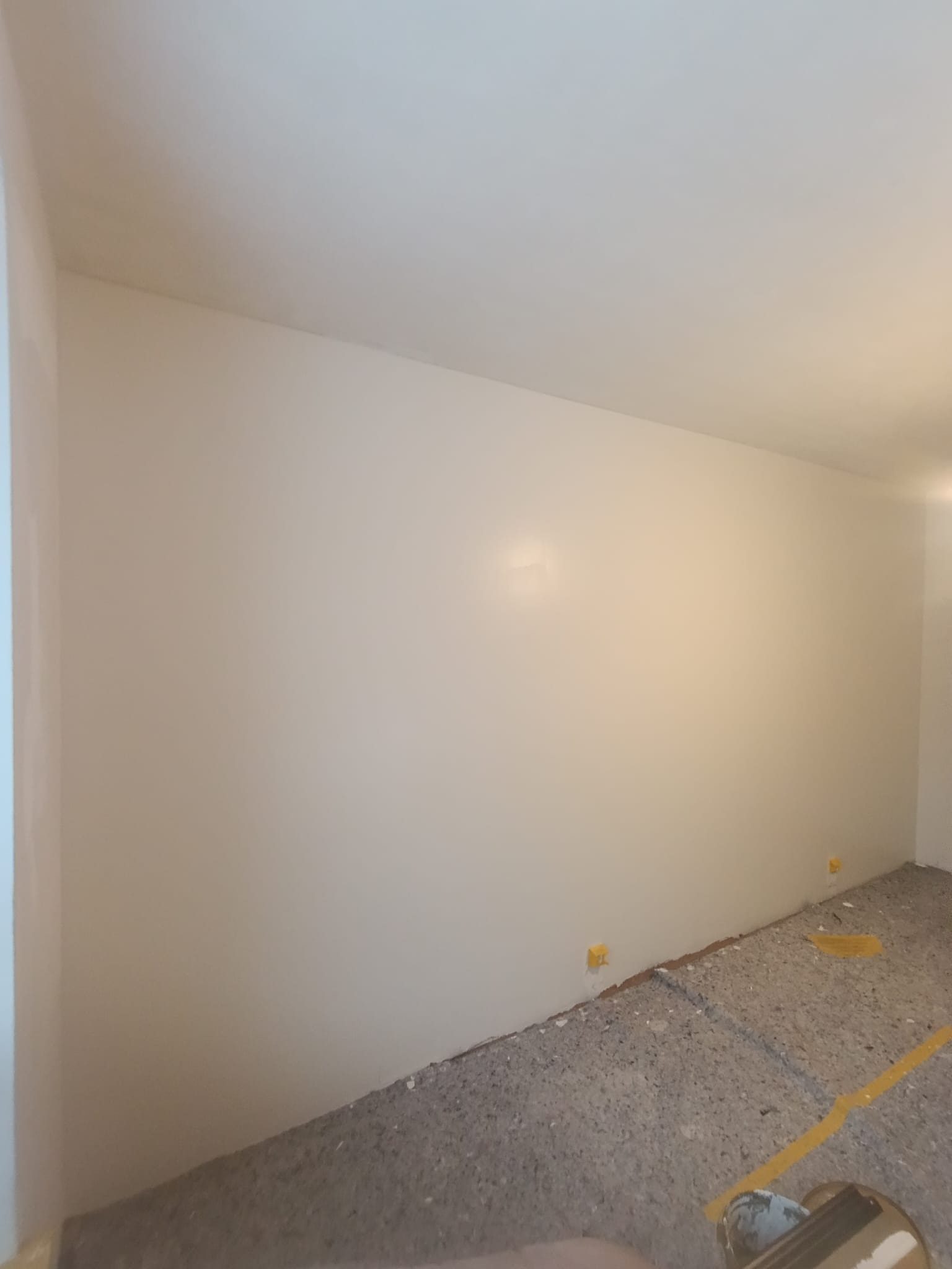 Świeżo pomalowane ściany w jasnym odcieniu, widoczne żółte zabezpieczenia podłogi i listew przypodłogowych. Minimalistyczne wnętrze po malowaniu.