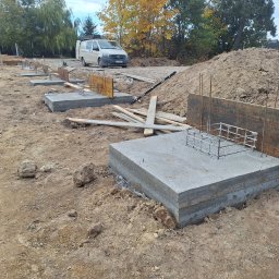 USŁUGI OGÓLNOBUDOWLANE - KAMIL KOBIELA - Wylane fundamenty pod budowę domu z widocznym zbrojeniem i szalunkiem. W tle zaparkowany biały bus i drzewa z jesiennymi liśćmi.